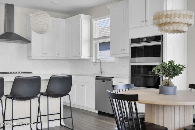 kitchen featuring a breakfast bar, light countertops, appliances with stainless steel finishes, wall chimney range hood, and wood finished floors