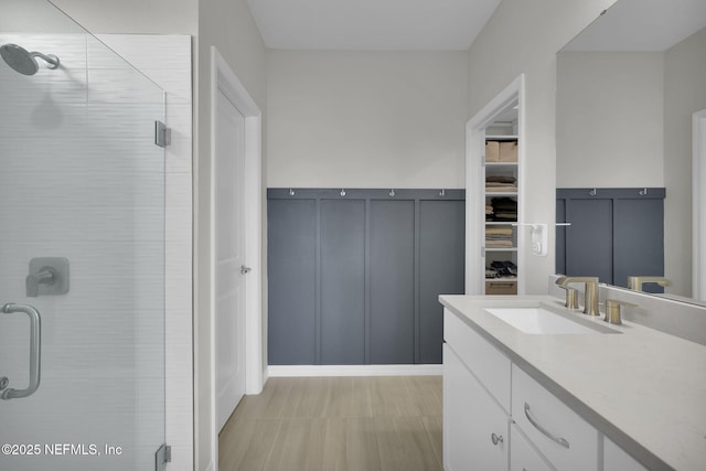 bathroom featuring a spacious closet, a shower stall, vanity, and a decorative wall