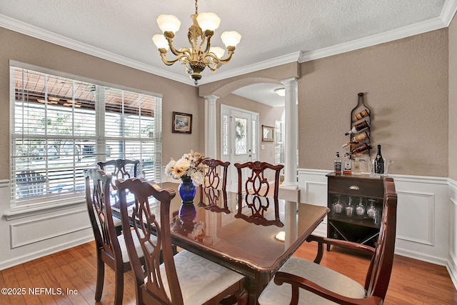 dining space featuring crown molding, ornate columns, a textured ceiling, and hardwood / wood-style floors