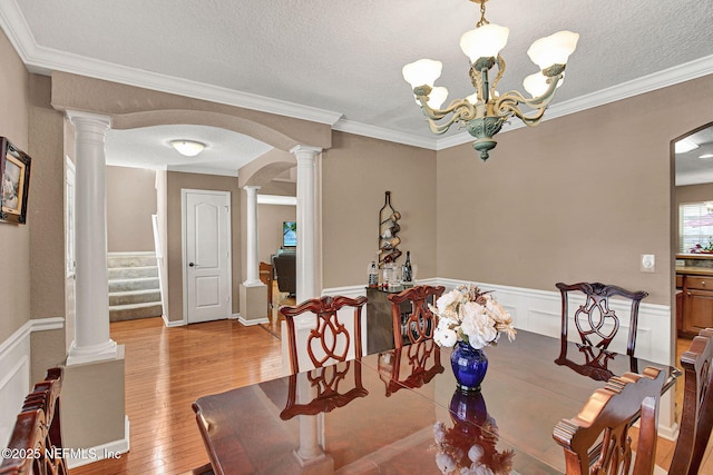 dining area with a textured ceiling, a chandelier, crown molding, light wood-type flooring, and decorative columns
