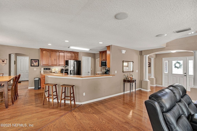 kitchen featuring appliances with stainless steel finishes, a breakfast bar, light wood-type flooring, decorative columns, and kitchen peninsula