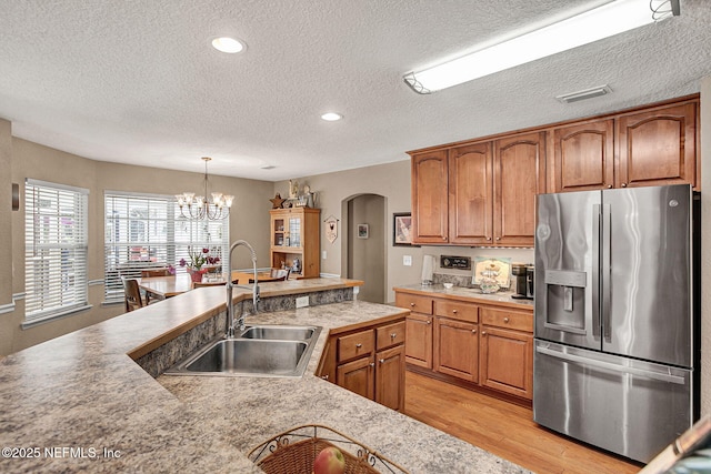 kitchen featuring an inviting chandelier, sink, light wood-type flooring, stainless steel fridge with ice dispenser, and hanging light fixtures