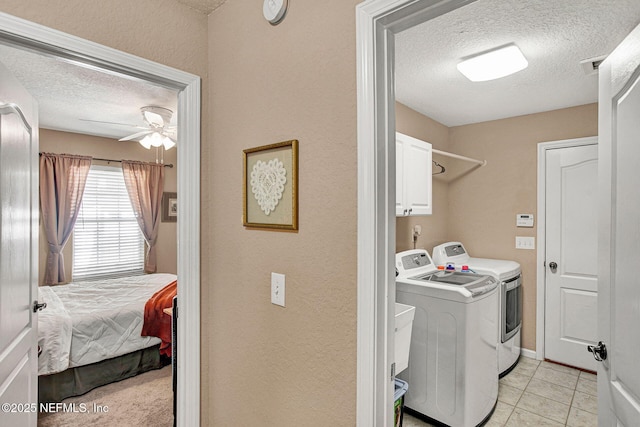 clothes washing area with washing machine and clothes dryer, a textured ceiling, ceiling fan, light tile patterned floors, and cabinets