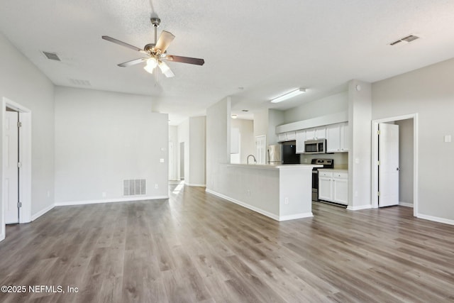 unfurnished living room with ceiling fan, visible vents, baseboards, and wood finished floors