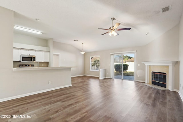 unfurnished living room with visible vents, a ceiling fan, wood finished floors, a high end fireplace, and vaulted ceiling