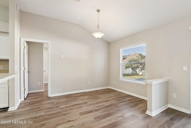 unfurnished dining area with vaulted ceiling, wood finished floors, and baseboards