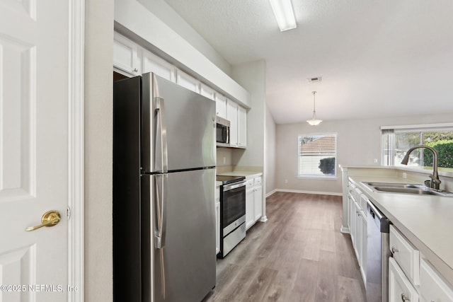 kitchen with light wood-style flooring, a sink, light countertops, appliances with stainless steel finishes, and white cabinetry