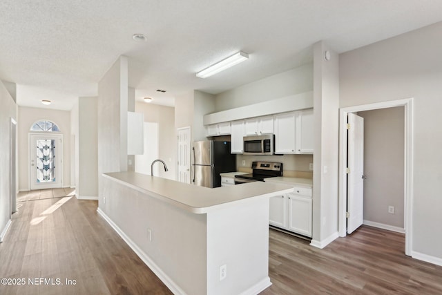 kitchen with white cabinetry, stainless steel appliances, light countertops, and wood finished floors