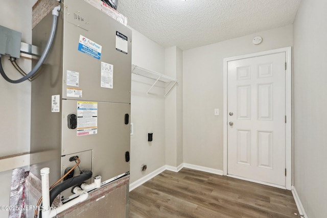 washroom with heating unit, a textured ceiling, wood finished floors, baseboards, and laundry area