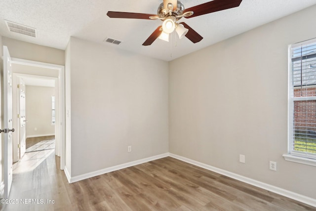 empty room with light wood-style flooring, plenty of natural light, and visible vents