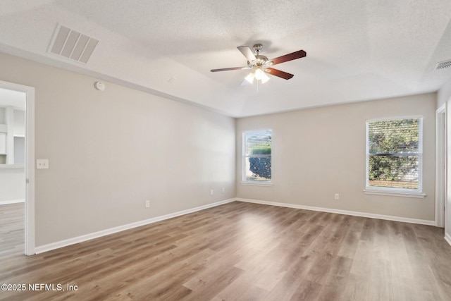 empty room with visible vents, a ceiling fan, a textured ceiling, wood finished floors, and a raised ceiling