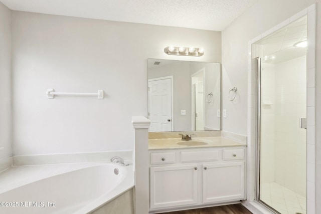 bathroom featuring a stall shower, a textured ceiling, a bath, and vanity