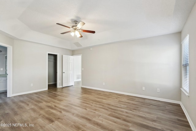 unfurnished bedroom with ceiling fan, baseboards, wood finished floors, a closet, and a raised ceiling