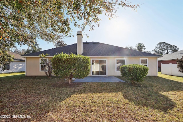 rear view of house with fence, stucco siding, a chimney, a yard, and a patio area