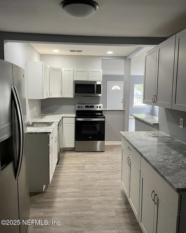 kitchen with beam ceiling, light hardwood / wood-style floors, stainless steel appliances, and white cabinetry