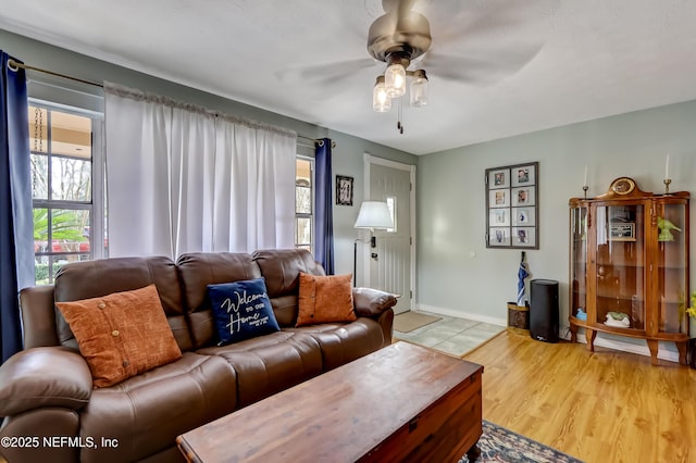 living area featuring a healthy amount of sunlight, light wood-style floors, ceiling fan, and baseboards