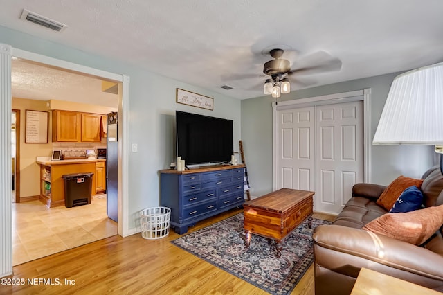 living room with light wood-style flooring, visible vents, ceiling fan, and a textured ceiling