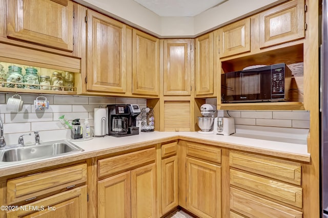 kitchen featuring black microwave, light countertops, a sink, and decorative backsplash