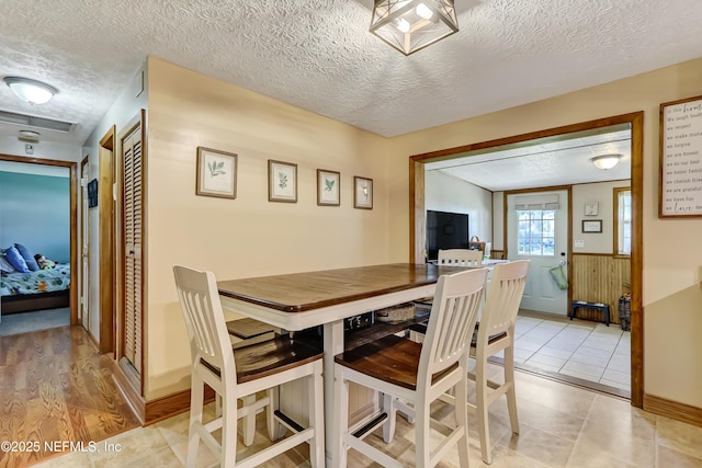 dining area featuring a textured ceiling, a wainscoted wall, and light tile patterned flooring