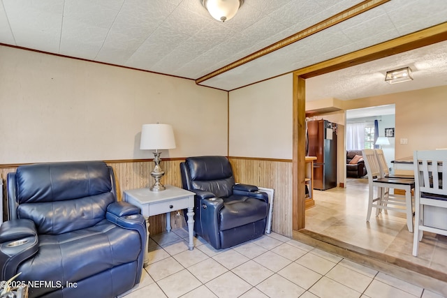 living area featuring crown molding, wainscoting, wooden walls, a textured ceiling, and tile patterned floors