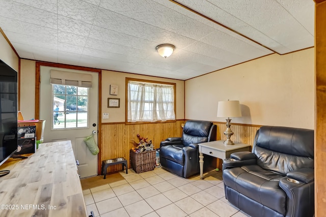 sitting room featuring a wainscoted wall, wooden walls, light tile patterned floors, and crown molding