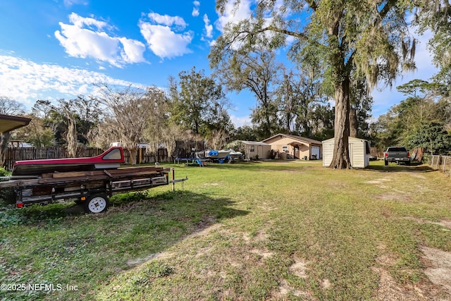 view of yard with a storage shed, a trampoline, fence, and an outbuilding