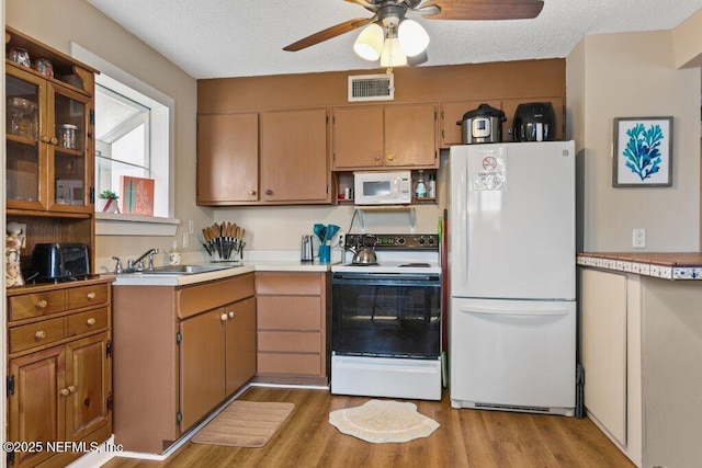 kitchen featuring white appliances, light wood-style flooring, brown cabinets, light countertops, and a sink