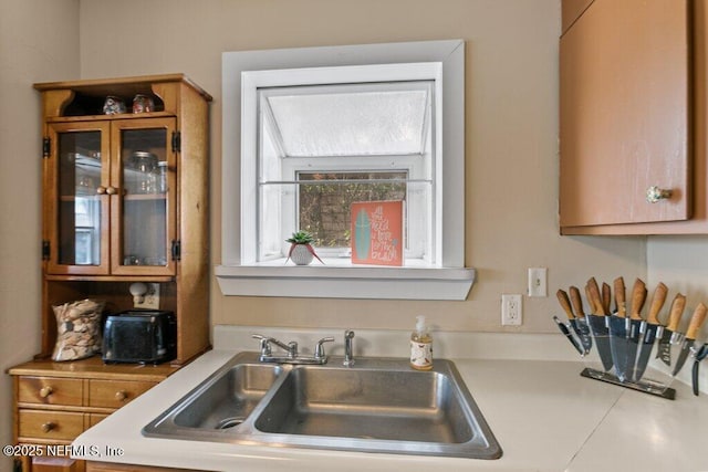 kitchen featuring light countertops, a sink, glass insert cabinets, and brown cabinets