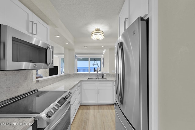 kitchen with appliances with stainless steel finishes, white cabinetry, a sink, recessed lighting, and light wood finished floors