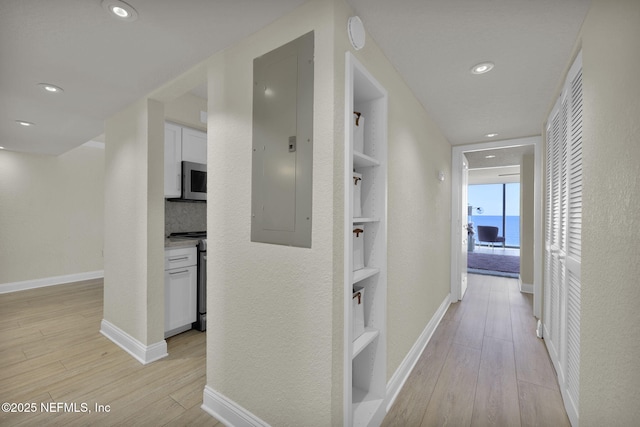 hallway featuring electric panel, light wood finished floors, baseboards, and recessed lighting