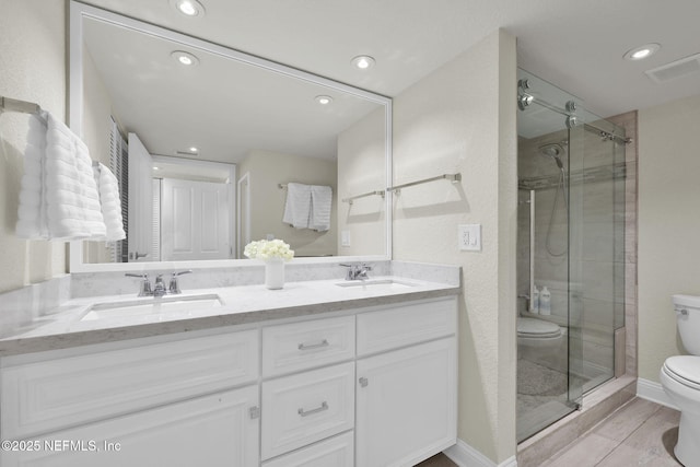 bathroom with toilet, a shower stall, double vanity, recessed lighting, and wood finished floors