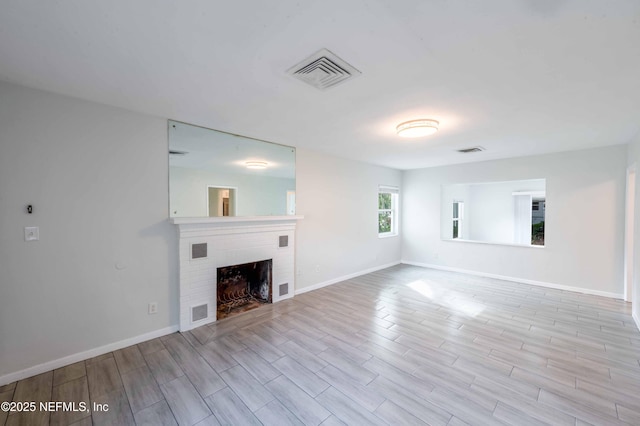 unfurnished living room featuring light wood finished floors, baseboards, a fireplace, and visible vents