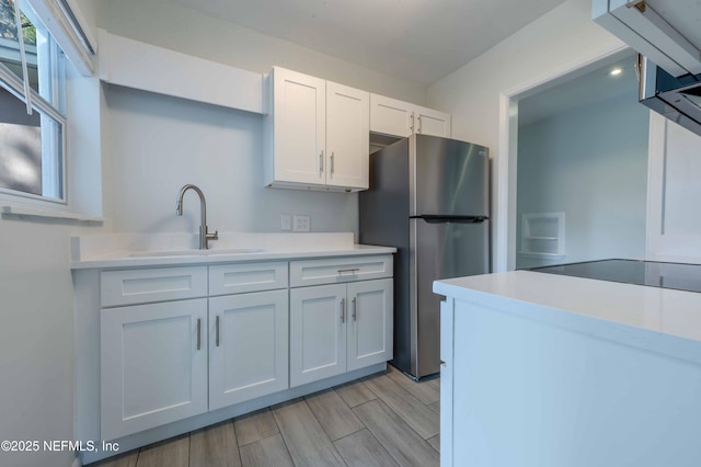 kitchen featuring freestanding refrigerator, light countertops, a sink, and white cabinetry