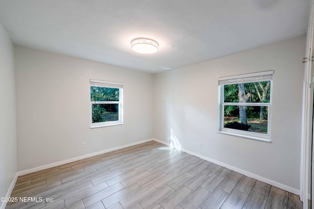 spare room with light wood-type flooring, a healthy amount of sunlight, and baseboards