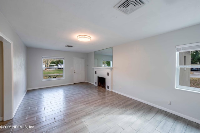 unfurnished living room with light wood-style floors, visible vents, a fireplace, and baseboards