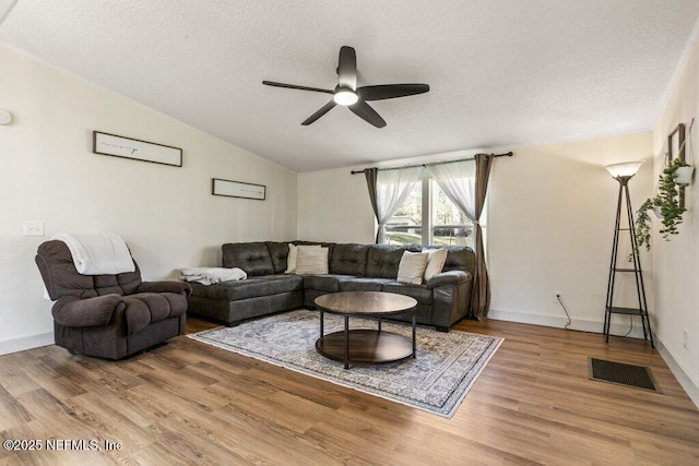 living area featuring light wood finished floors, visible vents, a ceiling fan, vaulted ceiling, and a textured ceiling