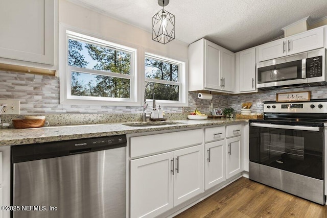 kitchen with stainless steel appliances, white cabinets, decorative light fixtures, and light stone counters