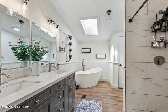 full bath with a freestanding tub, a skylight, a sink, and wood finished floors