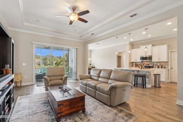 living room featuring light wood-style floors, a tray ceiling, visible vents, and crown molding