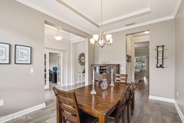 dining room featuring baseboards, visible vents, a tray ceiling, and wood finished floors