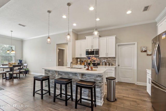 kitchen featuring tasteful backsplash, visible vents, stainless steel appliances, light countertops, and a kitchen bar