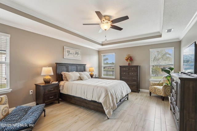 bedroom with light wood finished floors, a raised ceiling, visible vents, and baseboards