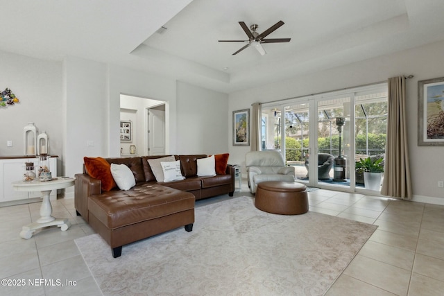 living room with light tile patterned floors, baseboards, a tray ceiling, and a ceiling fan