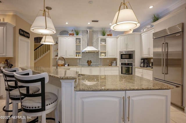 kitchen with visible vents, decorative backsplash, a sink, wall chimney range hood, and built in appliances