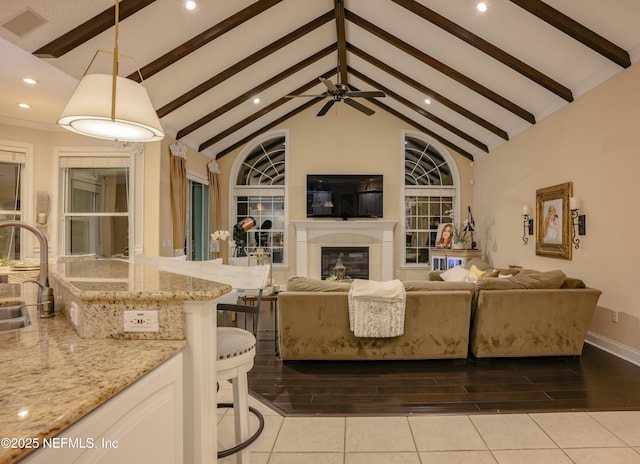 living room featuring high vaulted ceiling, light tile patterned flooring, beamed ceiling, and a glass covered fireplace