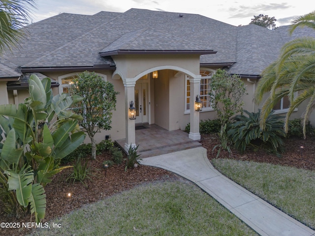 doorway to property with a shingled roof and stucco siding