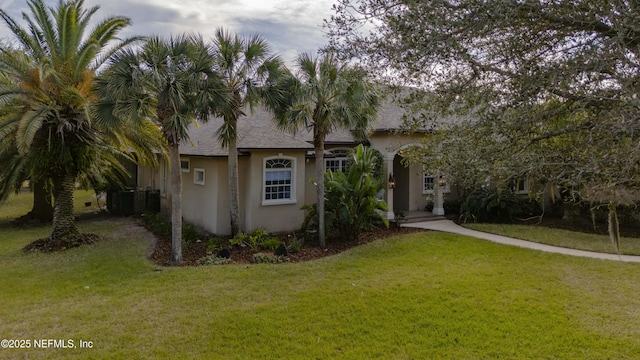 view of front facade featuring a shingled roof, a front lawn, and stucco siding