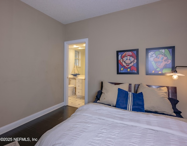 bedroom with ensuite bathroom, wood finished floors, and baseboards