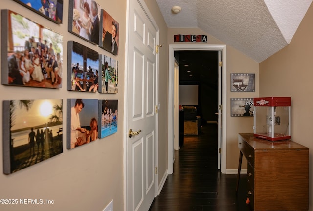 hallway featuring dark wood-type flooring, vaulted ceiling, a textured ceiling, and baseboards