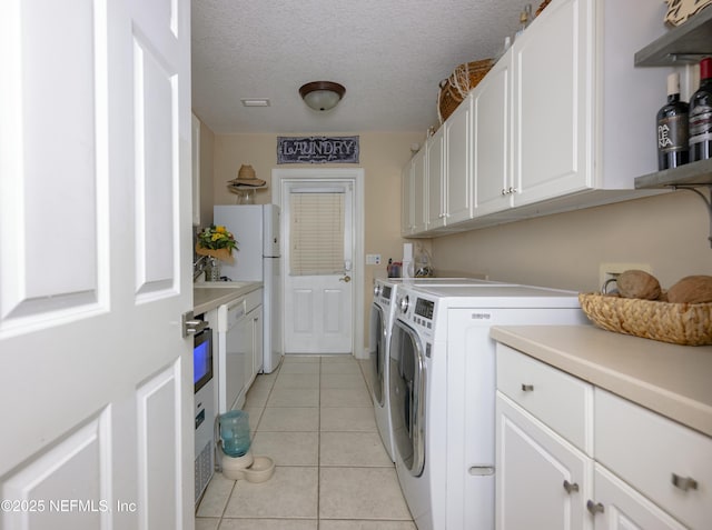 washroom with light tile patterned floors, a textured ceiling, independent washer and dryer, and cabinet space